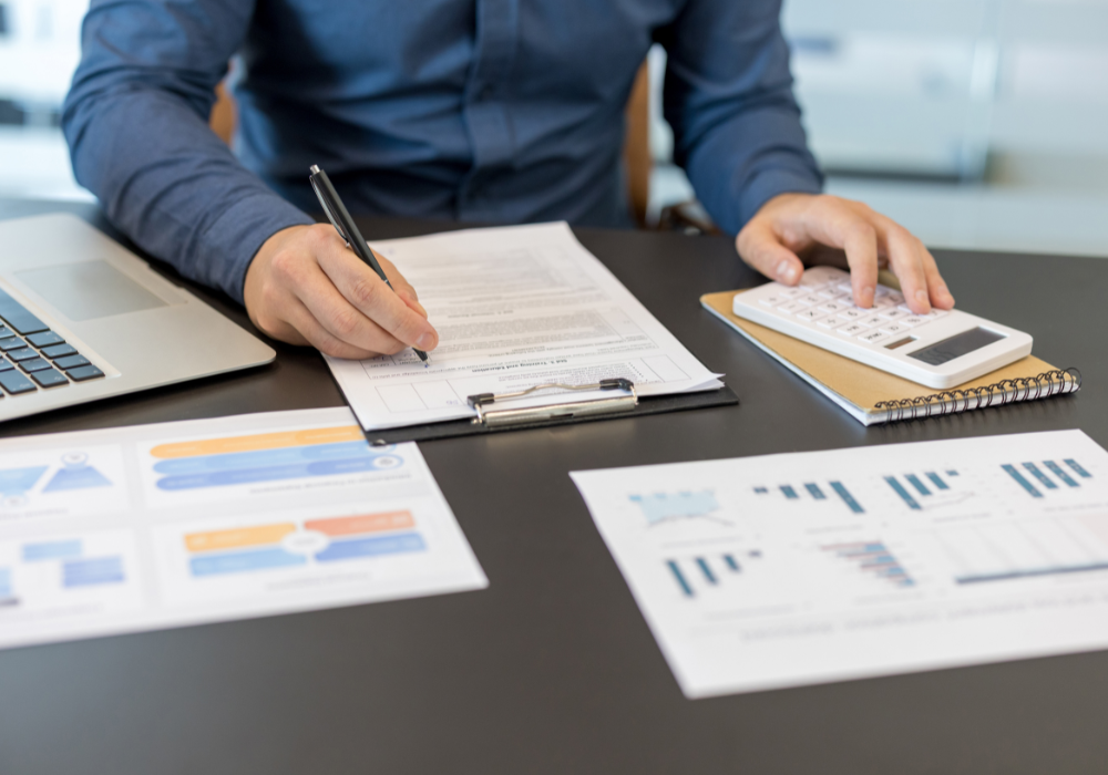 A professional using a calculator and reviewing budget documents and charts for an enterprise automation investment.